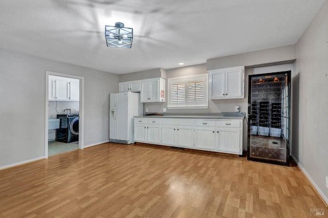 kitchen featuring washer / dryer, white refrigerator with ice dispenser, baseboards, white cabinets, and light wood-style floors