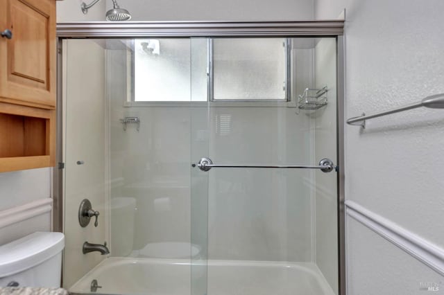 bathroom featuring toilet and bath / shower combo with glass door