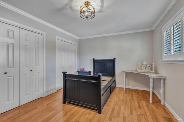 bedroom with light wood-style floors, crown molding, baseboards, and multiple closets