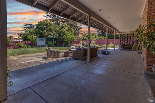 patio terrace at dusk with a fenced backyard, an outdoor hangout area, and a lawn