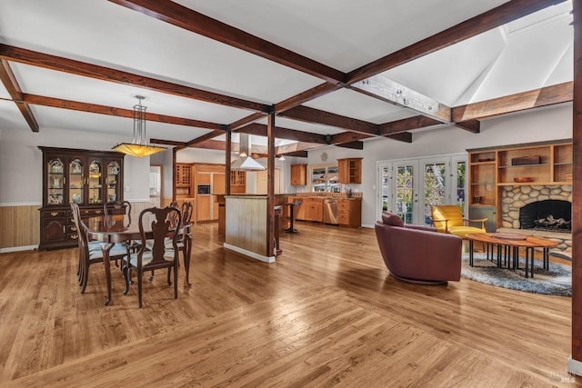 dining room featuring a wainscoted wall, a stone fireplace, french doors, and wood finished floors