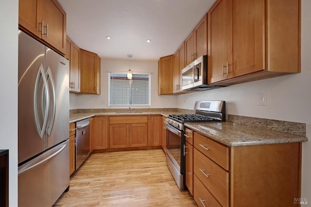 kitchen with decorative light fixtures, sink, light stone counters, stainless steel appliances, and light wood-type flooring