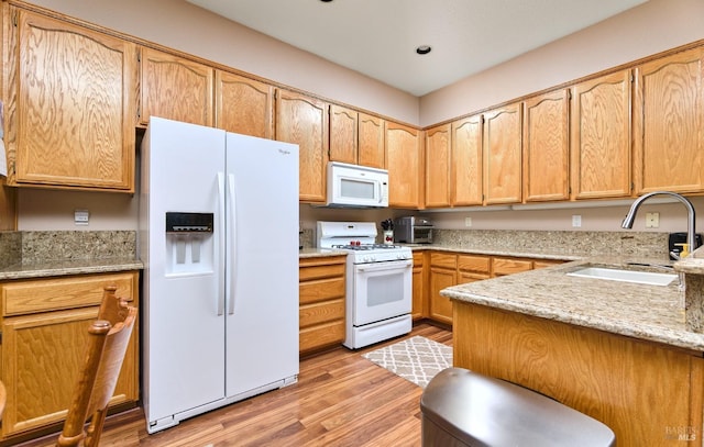 kitchen featuring light stone counters, white appliances, a sink, and light wood finished floors