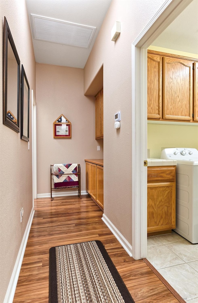 corridor with visible vents, light wood finished floors, washer / dryer, and baseboards