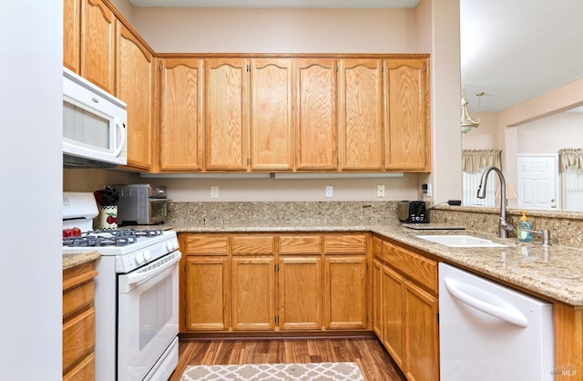 kitchen with a peninsula, white appliances, a sink, light wood-style floors, and light stone countertops