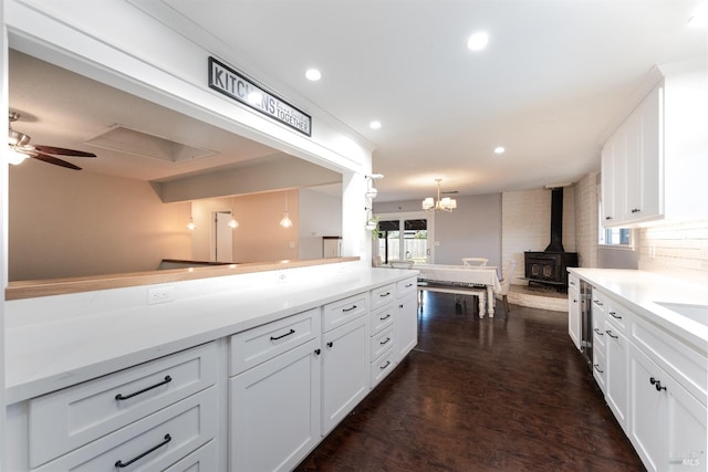 kitchen with tasteful backsplash, white cabinets, ceiling fan with notable chandelier, decorative light fixtures, and a wood stove