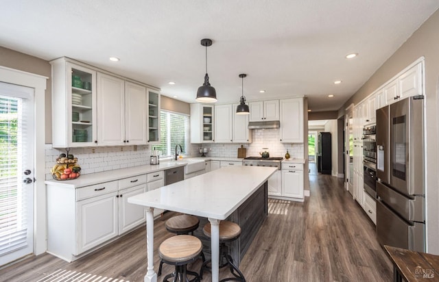 kitchen with light countertops, appliances with stainless steel finishes, a kitchen island, and glass insert cabinets