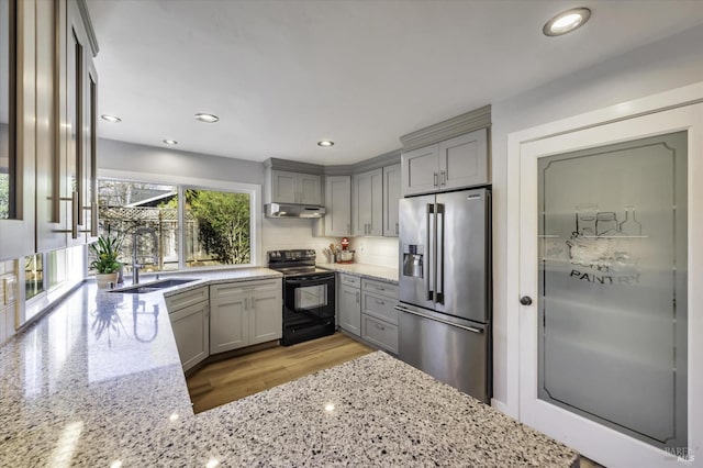 kitchen featuring sink, black electric range, high end refrigerator, and light stone countertops