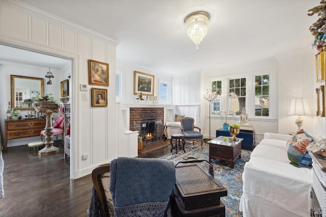 living room featuring dark wood-type flooring, a fireplace, a chandelier, and crown molding