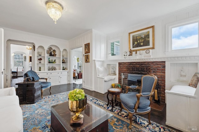 living room featuring dark hardwood / wood-style floors, a fireplace, ornamental molding, an inviting chandelier, and built in shelves