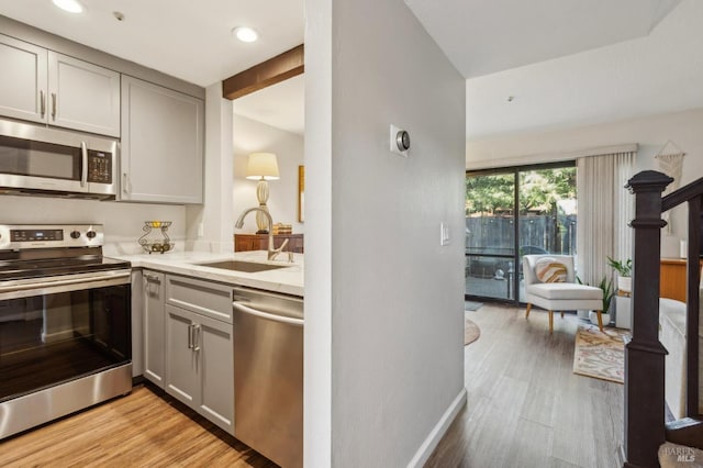 kitchen featuring light wood-style floors, appliances with stainless steel finishes, a sink, and gray cabinetry