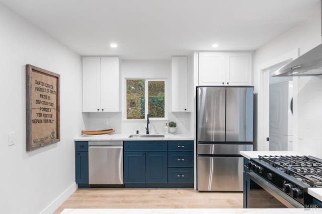 kitchen with blue cabinets, sink, appliances with stainless steel finishes, white cabinets, and wall chimney range hood