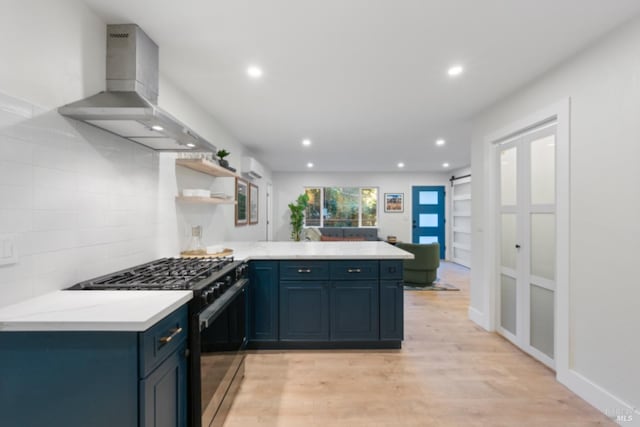 kitchen featuring gas range, kitchen peninsula, a barn door, light hardwood / wood-style floors, and wall chimney range hood