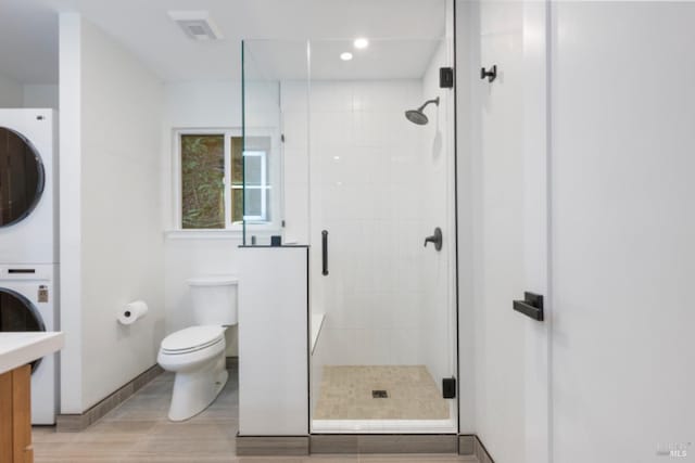 bathroom with stacked washer and dryer, vanity, a shower with shower door, and toilet