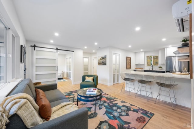 living room featuring sink, a barn door, light hardwood / wood-style floors, and a wall unit AC