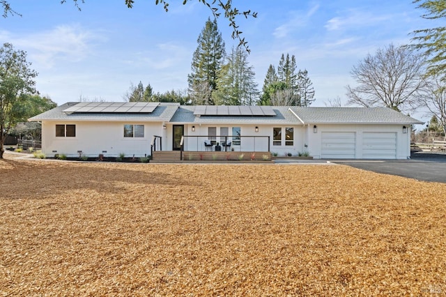 view of front of property featuring aphalt driveway, roof mounted solar panels, and an attached garage