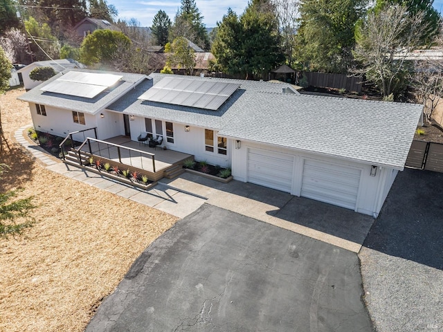 view of front of property featuring a shingled roof, aphalt driveway, a wooden deck, and solar panels