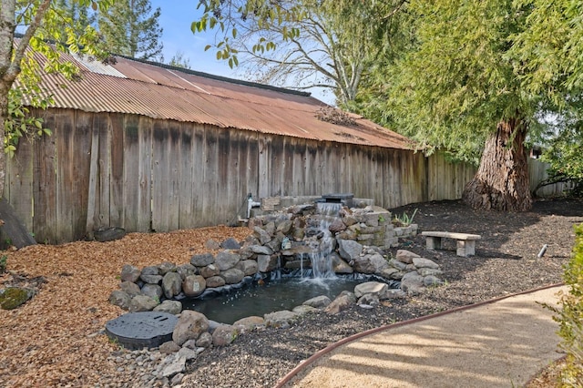 view of side of home featuring metal roof, a small pond, and fence