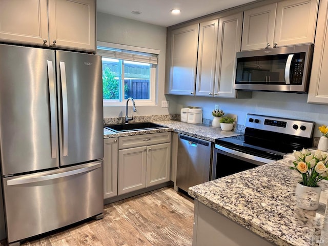 kitchen featuring sink, gray cabinets, stainless steel appliances, light stone counters, and light hardwood / wood-style floors