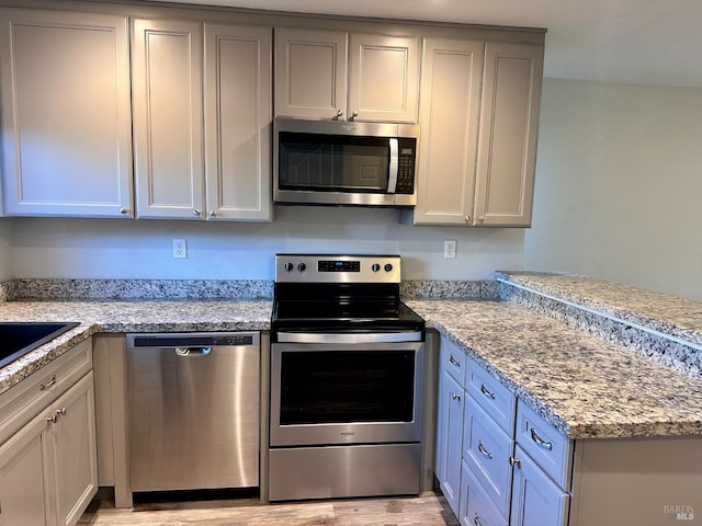 kitchen with light stone counters, stainless steel appliances, and light hardwood / wood-style flooring