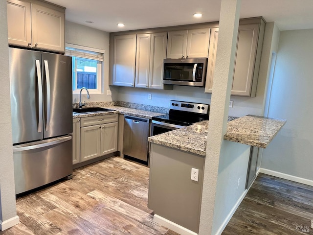 kitchen with sink, light stone countertops, light hardwood / wood-style floors, and appliances with stainless steel finishes