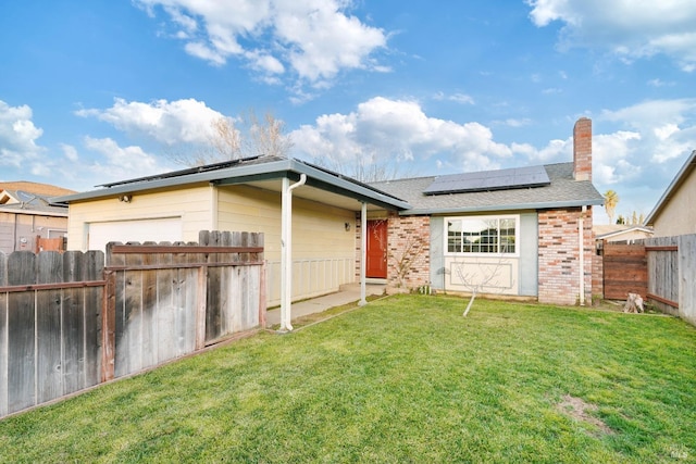 rear view of property featuring a lawn and solar panels