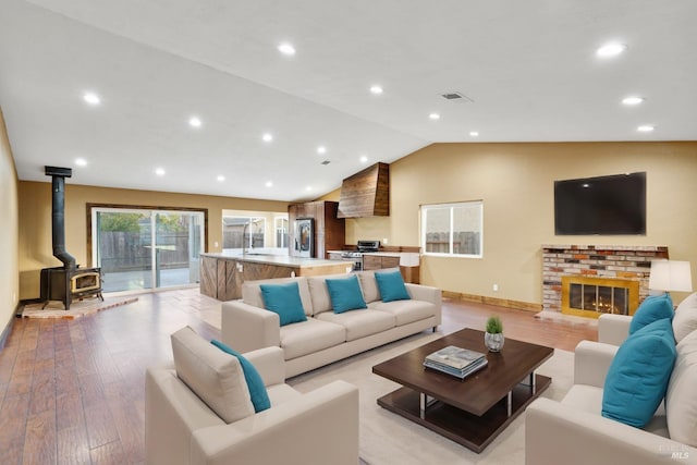 living room with a wood stove, a brick fireplace, light hardwood / wood-style flooring, sink, and vaulted ceiling