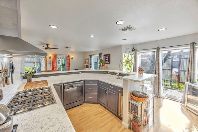 kitchen with light stone countertops, appliances with stainless steel finishes, island range hood, and kitchen peninsula