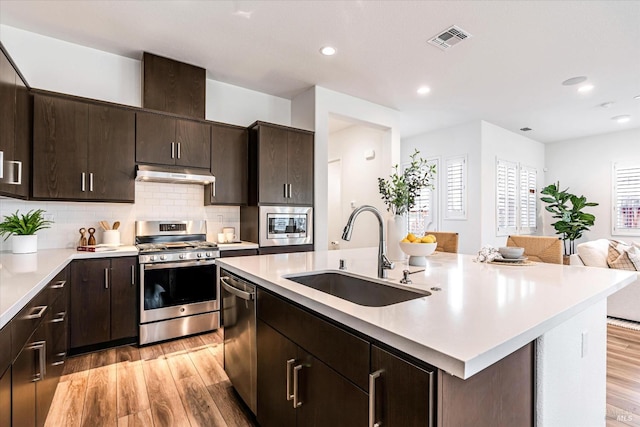 kitchen featuring a center island with sink, visible vents, appliances with stainless steel finishes, under cabinet range hood, and a sink