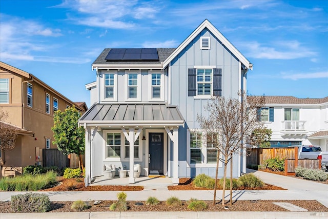 modern inspired farmhouse featuring a standing seam roof, fence, roof mounted solar panels, a porch, and board and batten siding