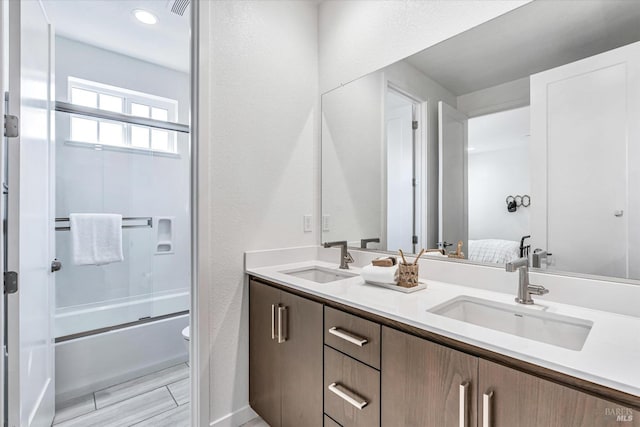 full bathroom with combined bath / shower with glass door, a sink, toilet, and double vanity