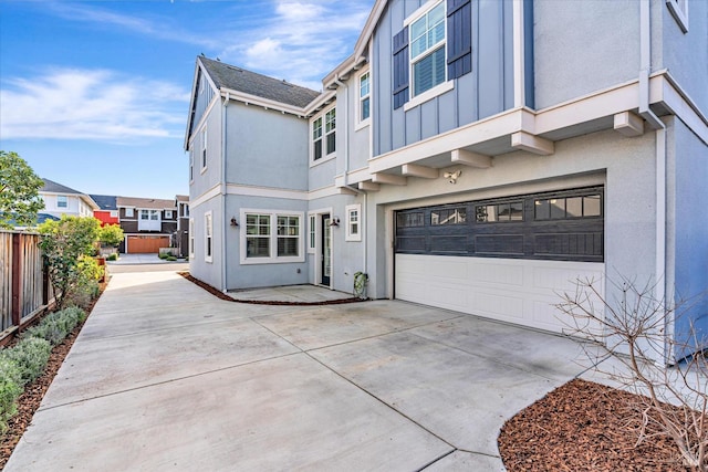 view of front of home featuring stucco siding, concrete driveway, board and batten siding, fence, and a garage