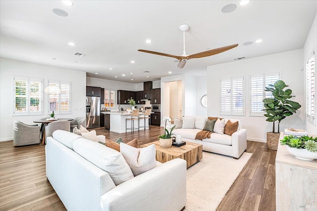 living room featuring light wood-style flooring, visible vents, baseboards, and recessed lighting