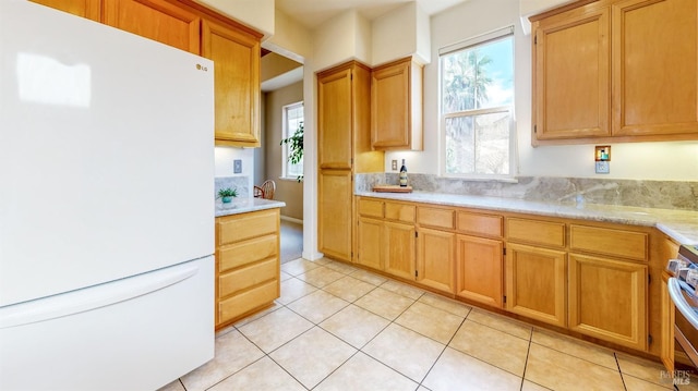 kitchen featuring light tile patterned floors, stainless steel stove, plenty of natural light, and white refrigerator