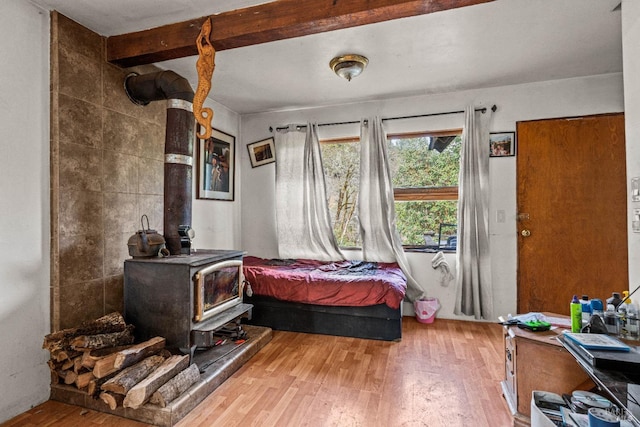 bedroom with beamed ceiling, wood-type flooring, and a wood stove