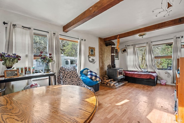 dining area with beam ceiling, wood-type flooring, plenty of natural light, and a wood stove