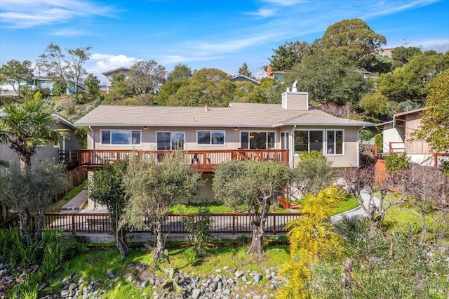 rear view of property featuring a wooden deck, fence, a chimney, and stucco siding