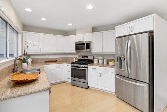 kitchen with sink, appliances with stainless steel finishes, light stone counters, light hardwood / wood-style floors, and white cabinets