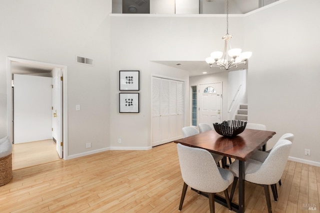 dining space featuring hardwood / wood-style flooring, a towering ceiling, and an inviting chandelier