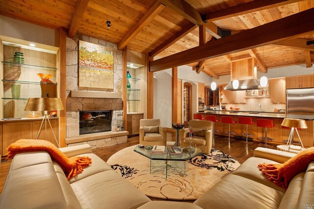 living room with wood ceiling, vaulted ceiling with beams, hardwood / wood-style flooring, and a stone fireplace