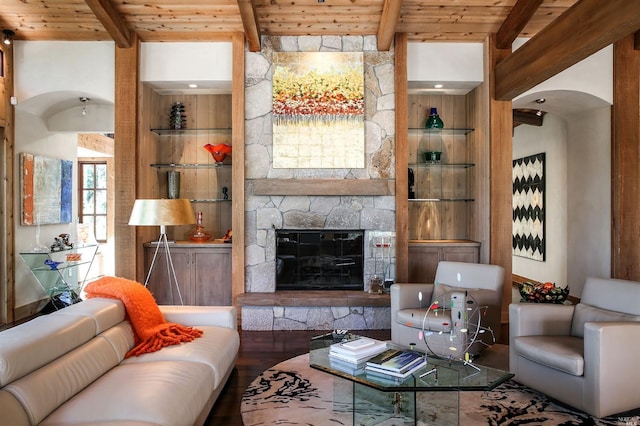 living room featuring beam ceiling, a stone fireplace, wood ceiling, and built in shelves