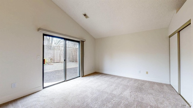 carpeted empty room featuring vaulted ceiling and a textured ceiling