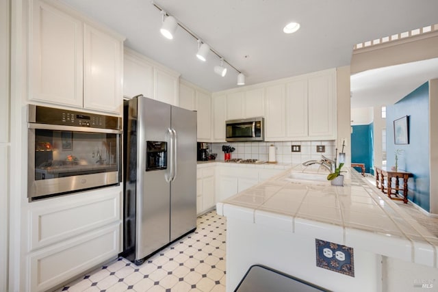 kitchen featuring tasteful backsplash, tile countertops, appliances with stainless steel finishes, light floors, and a sink