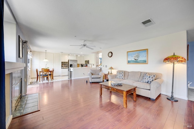 living area featuring ceiling fan, a fireplace, wood finished floors, visible vents, and baseboards