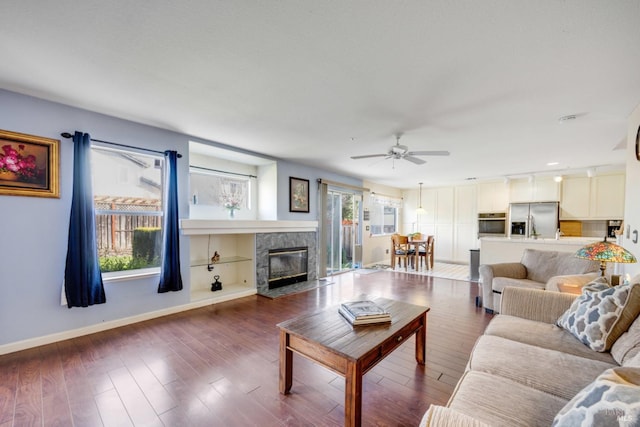 living area featuring a ceiling fan, a fireplace, baseboards, and wood finished floors