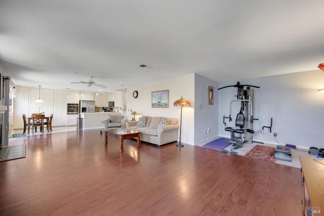 living area with baseboards, ceiling fan, visible vents, and wood finished floors