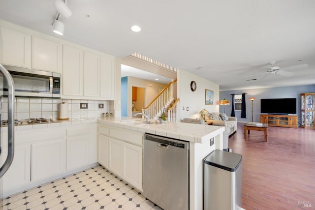 kitchen featuring tile countertops, a peninsula, a sink, appliances with stainless steel finishes, and light floors