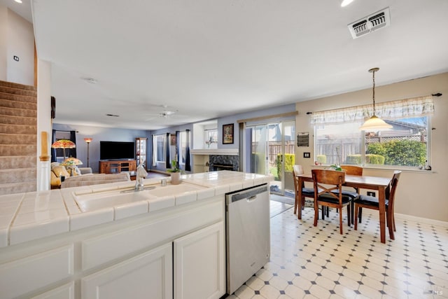 kitchen featuring visible vents, tile countertops, stainless steel dishwasher, a fireplace, and a sink