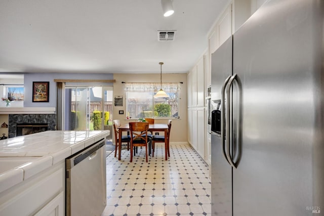 kitchen with tile countertops, stainless steel appliances, a premium fireplace, visible vents, and white cabinetry