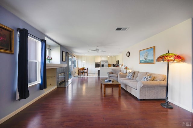 living area featuring a fireplace, visible vents, a ceiling fan, wood finished floors, and baseboards